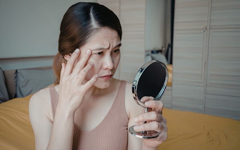 鏡を見て顔のたるみを気にする女性